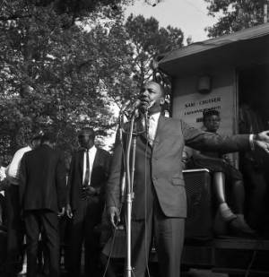 Martin Luther King Jr. addressing an audience at a voter rally in a wooded area in Alabama.