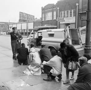 Fred Shuttlesworth and other civil rights demonstrators kneeling before a police officer during a protest march in downtown Birmingham, Alabama.