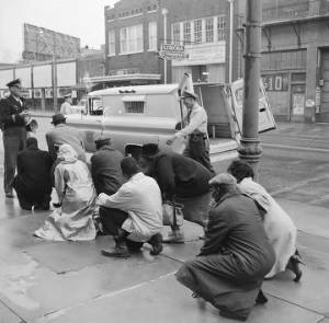Fred Shuttlesworth and other civil rights demonstrators kneeling before a police officer during a protest march in downtown Birmingham, Alabama.