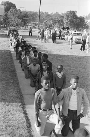 Young African Americans kneeling on a sidewalk in the George Washington Carver Homes neighborhood in Selma, Alabama, during a civil rights demonstration.