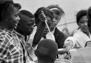 Young woman ladling water into paper cups for people standing around a table outside Harrison Street Baptist Church in Greenville, Alabama, during a student boycott of the Greenville Training School.