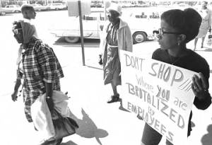 Young woman carrying a sign on the sidewalk outside the S. H. Kress & Co. department store on Dexter Avenue in downtown Montgomery, Alabama.