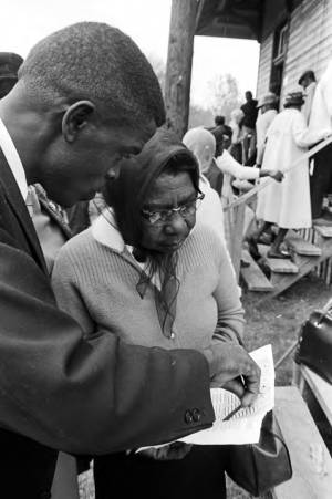 Man and woman looking over a sheet of paper (possibly a sample ballot) outside a building in Lowndes County, Alabama, on election day.