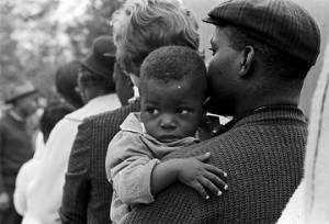 Man holding a baby while standing in line outside a building in Lowndes County, Alabama, on election day.