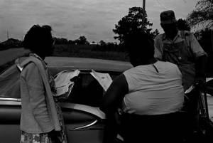 Two women talking to a man standing beside a car, while canvassing voters for the Lowndes County Freedom Organization.