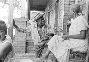 Collins Harris, a farmer and civil rights leader in Crenshaw County, Alabama, speaking to a woman on the front porch of a wooden house.