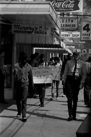 Protestors carrying signs while marching past Murphy's Prescription Drugs in downtown Prattville, Alabama, during a civil rights demonstration.