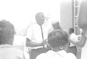 Dan Houser speaking to a group of people standing outside the First Missionary Baptist Church in Prattville, Alabama, during a meeting of the Autauga County Improvement Association.