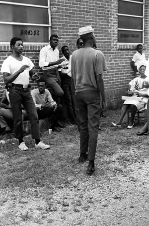 Man standing in front of an audience outside the First Missionary Baptist Church in Prattville, Alabama, during a meeting of the Autauga County Improvement Association.
