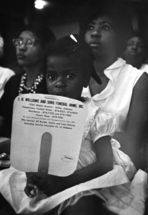 Little girl seated in a woman's lap in the audience at Brown Chapel AME Church in Selma, Alabama, during a civil rights meeting.