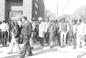 Wendell Paris and other students from Tuskegee Institute marching down a sidewalk beside the Alabama Exchange Bank, during a demonstration to protest the murder of Samuel L. Younge, a civil rights worker.