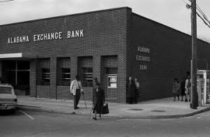 Woman crossing the street in front of the Alabama Exchange Bank in downtown Tuskegee, Alabama.