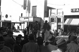 Willie Ricks standing on a car and addressing a crowd on the sidewalk in downtown Tuskegee, Alabama, during a student demonstration to protest the murder of Samuel L. Younge, a civil rights worker.
