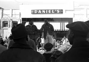 Willie Ricks standing on a car and addressing a crowd on the sidewalk in downtown Tuskegee, Alabama, during a student demonstration to protest the murder of Samuel L. Younge, a civil rights worker.