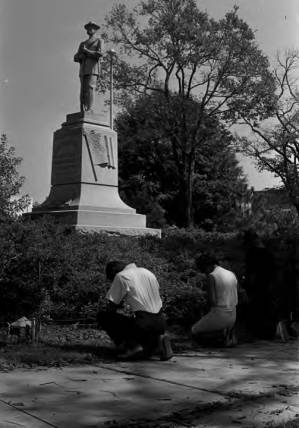 Young man and woman kneeling at the base of the Confederate monument in Tuskegee, Alabama, during a student demonstration to protest the verdict in the trial of Thomas Coleman, a Lowndes County man who had been charged with the murder of Jonathan Daniels.