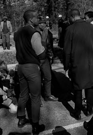 Students from Tuskegee Institute seated and standing in a road during a demonstration to protest the murder of Samuel L. Younge, a civil rights worker.