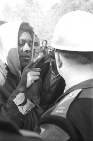 Simuel Schutz, Jr., speaking to policemen who have lined up across a road to block their demonstration in Tuskegee, Alabama, to protest the murder of Samuel L. Younge, a civil rights worker.