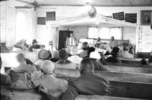 Man speaking to an audience in a small wooden church building in Prattville, Alabama, probably during a meeting of the Autauga County Voters Association.