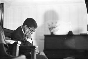 Young man sitting in a chair behind Martin Luther King, who is speaking to an audience at Tabernacle Baptist Church in Selma, Alabama.