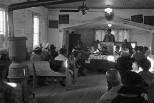 Norman Lumpkin speaking to an audience in a small wooden church building in Prattville, Alabama, probably during a meeting of the Autauga County Voters Association.