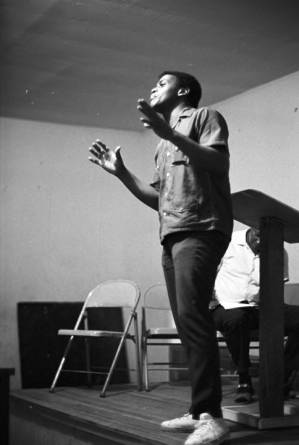 Latt Martin speaking on a small stage before a group of people.