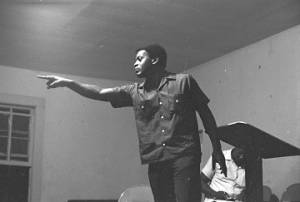 Latt Martin speaking on a small stage before a group of people.