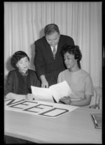 Man and two women examining documents at desk with large NEED [Negro Educational Emergency Drive] sign, another version