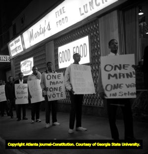 Demonstrators hold signs with 'One Man, One Vote' while Gov. George Wallace visits Atlanta, 1963