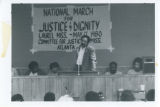 James Orange speaks in front of banner for "National March for Justice & Dignity"