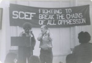 Two people speak a microphone by podium