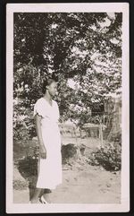 [Unidentified woman, wearing white dress, standing in yard] [graphic].