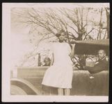 [Young woman standing on running board of car with man sitting behind steering wheel, and woman standing on opposide side of car] [graphic].