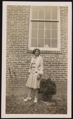 [Young woman posing for photograph in front of brick wall] [graphic].