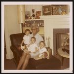 [Woman sitting on chair, in living room, holding three toddlers] [graphic].